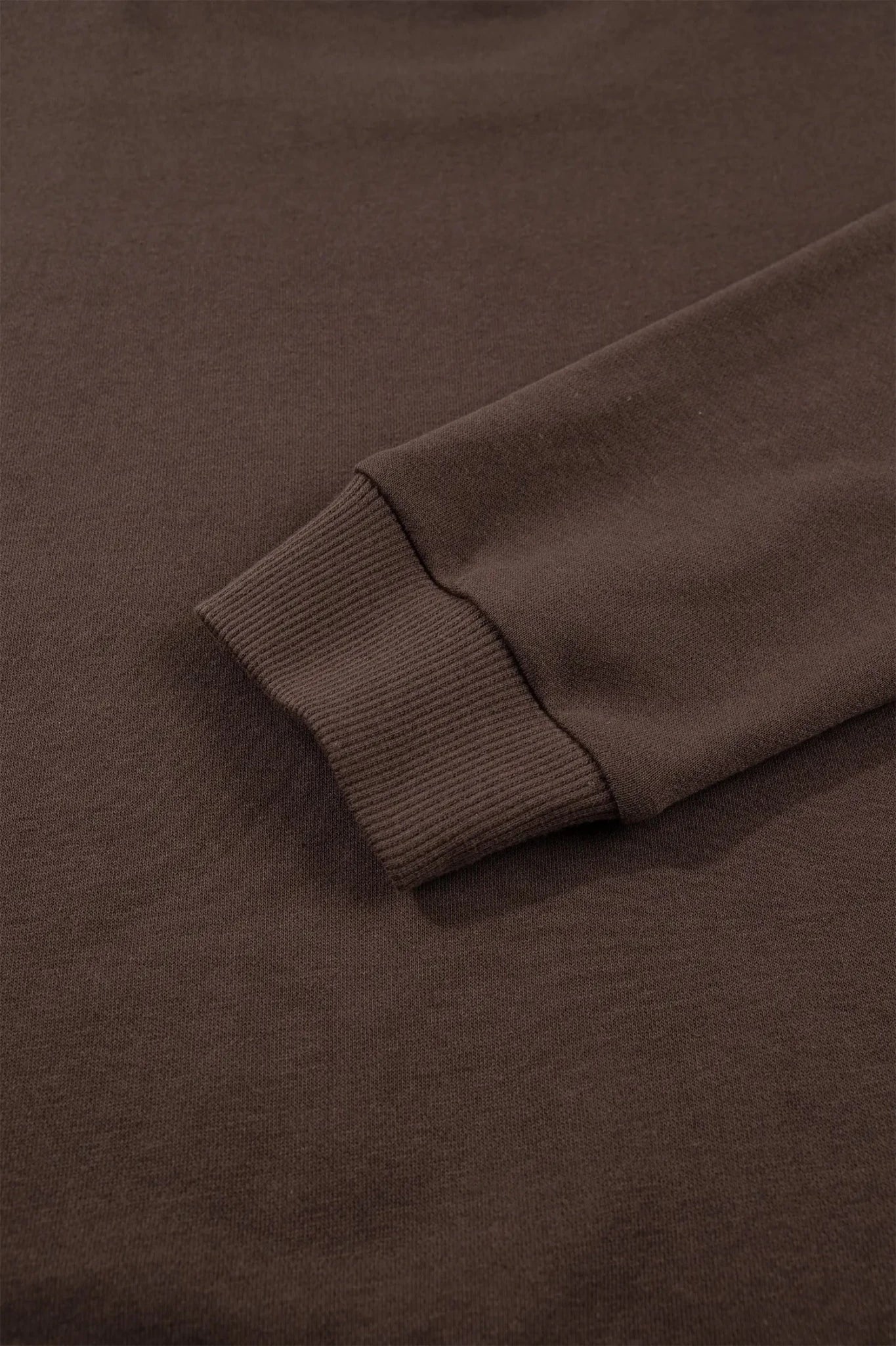 Close-up of a dark brown ribbed knit fabric, showing the texture and a folded cuff detail.