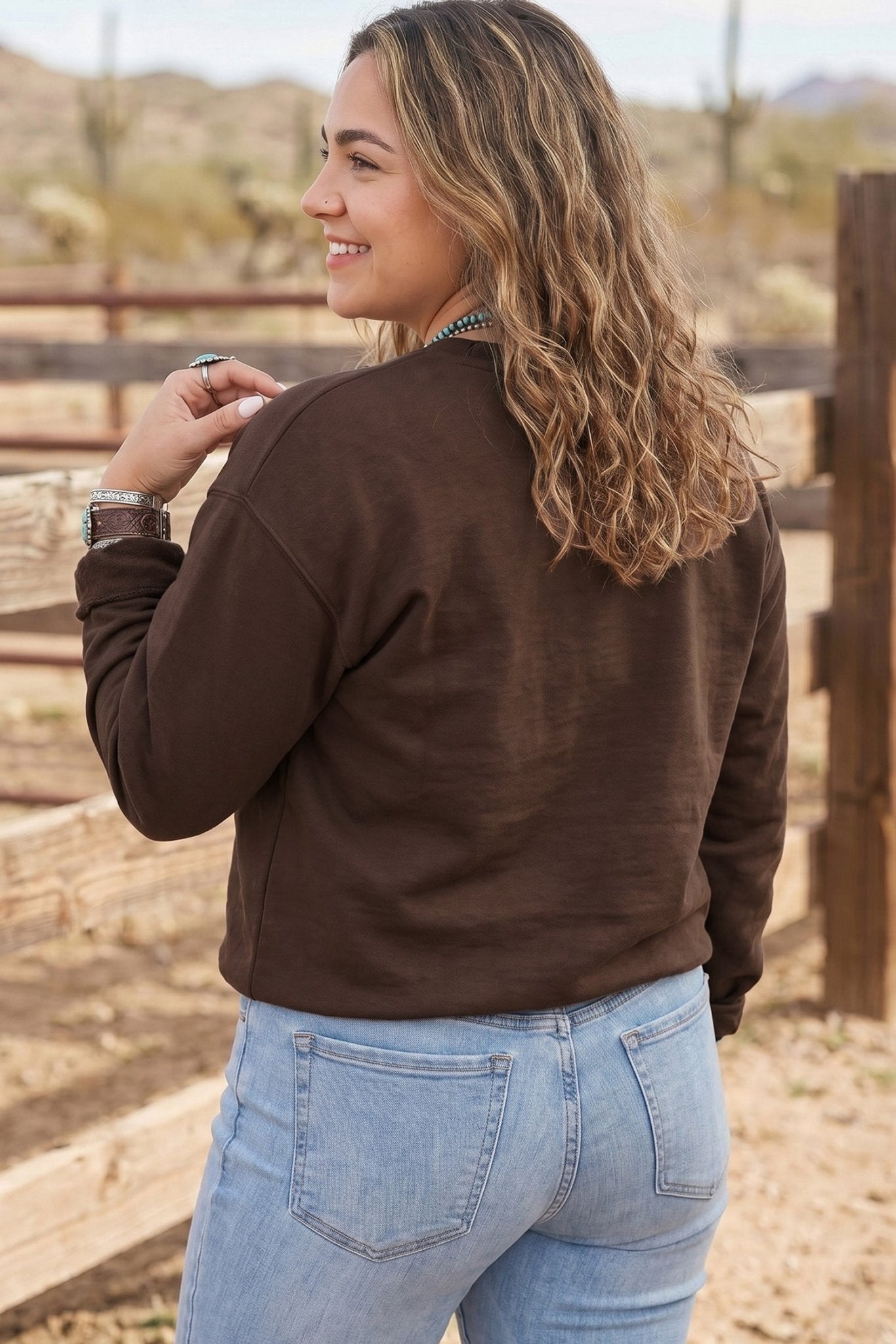 Back view of woman in dark brown cropped sweatshirt and light blue jeans outdoors.