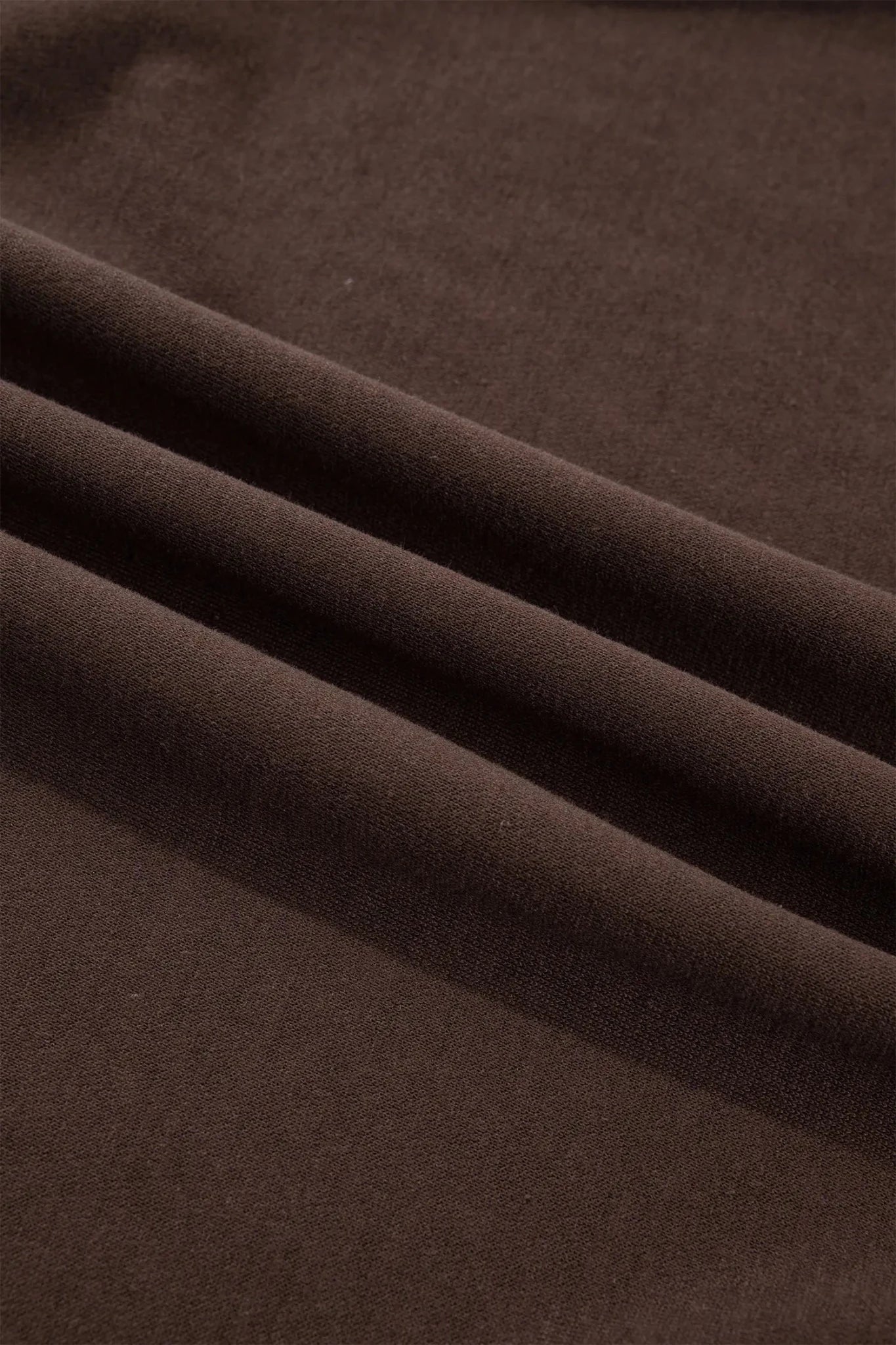 A close-up of draped dark brown fabric with soft folds showing its texture and color.