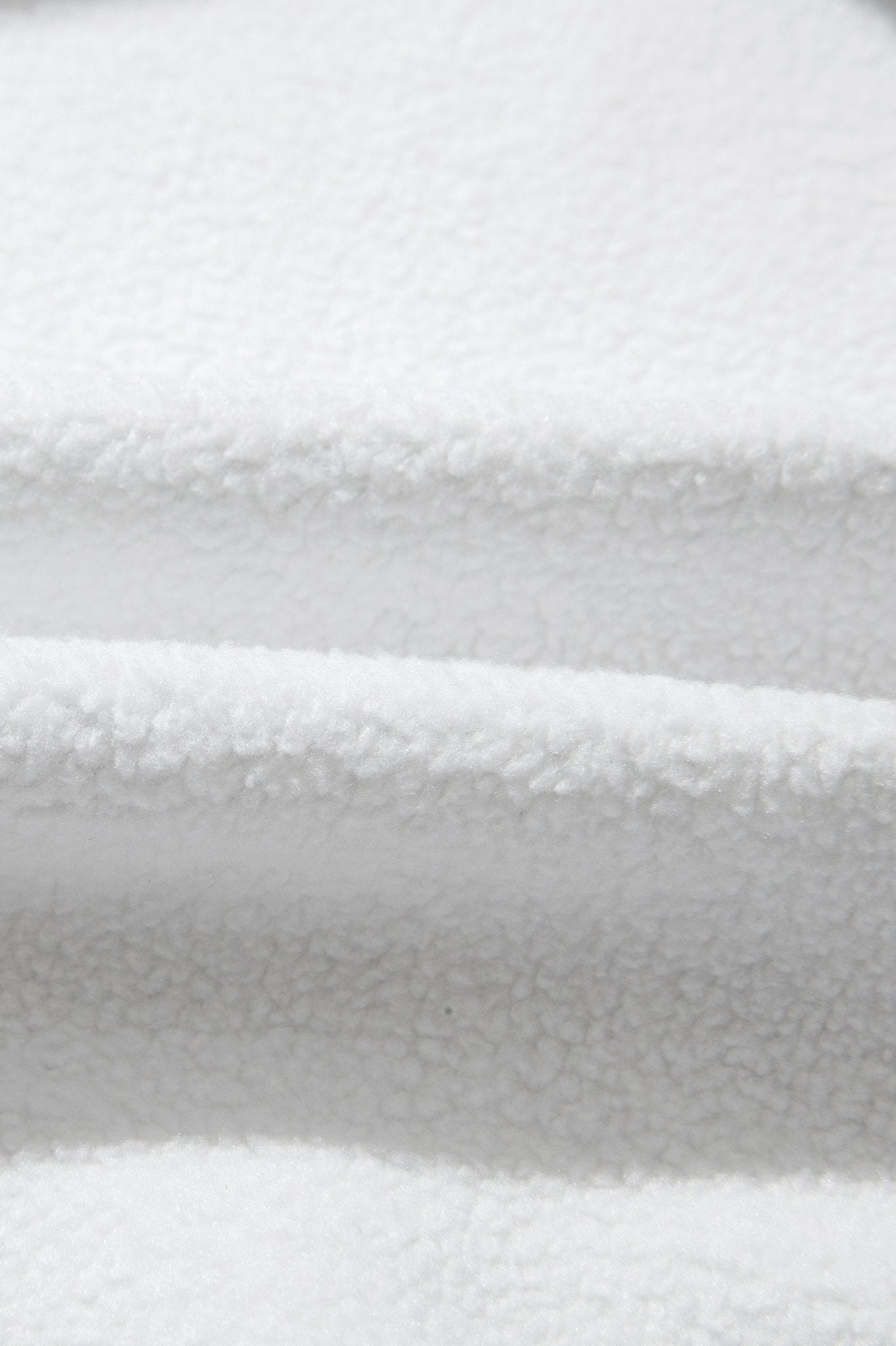 A close-up of white plush fleece fabric with soft folds and a textured sherpa-like surface.