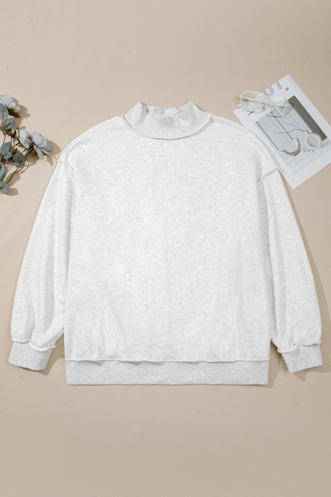 Light gray heathered mock neck sweatshirt with ribbed cuffs and hem, flat on beige with dried flowers and car