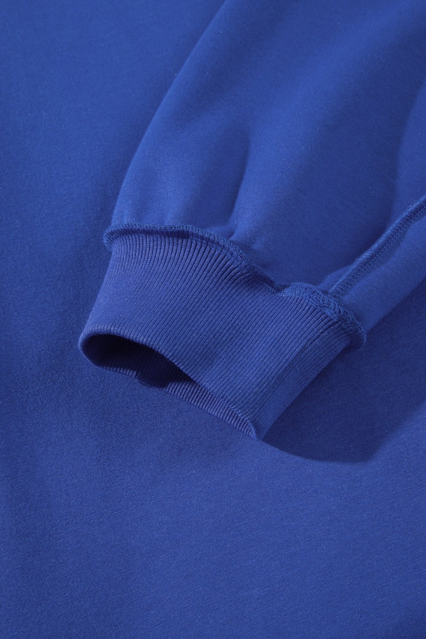 Close-up of a royal blue sweatshirt sleeve with a ribbed cuff, showing the fabric texture and stitching.