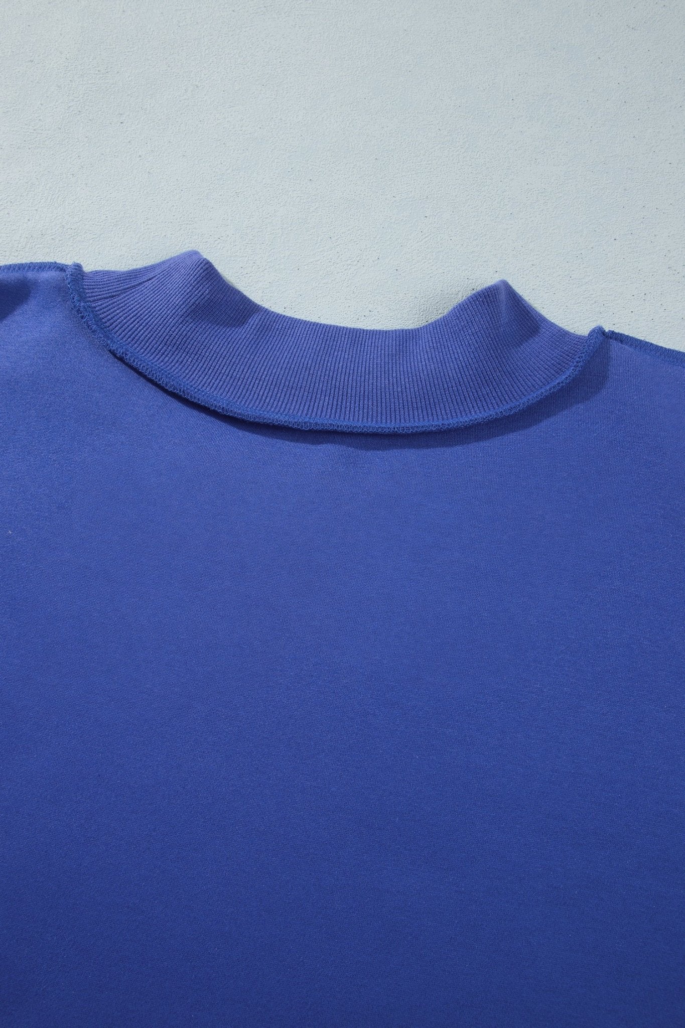 Close-up of royal blue crewneck sweatshirt with ribbed collar and smooth fabric texture on light gray.