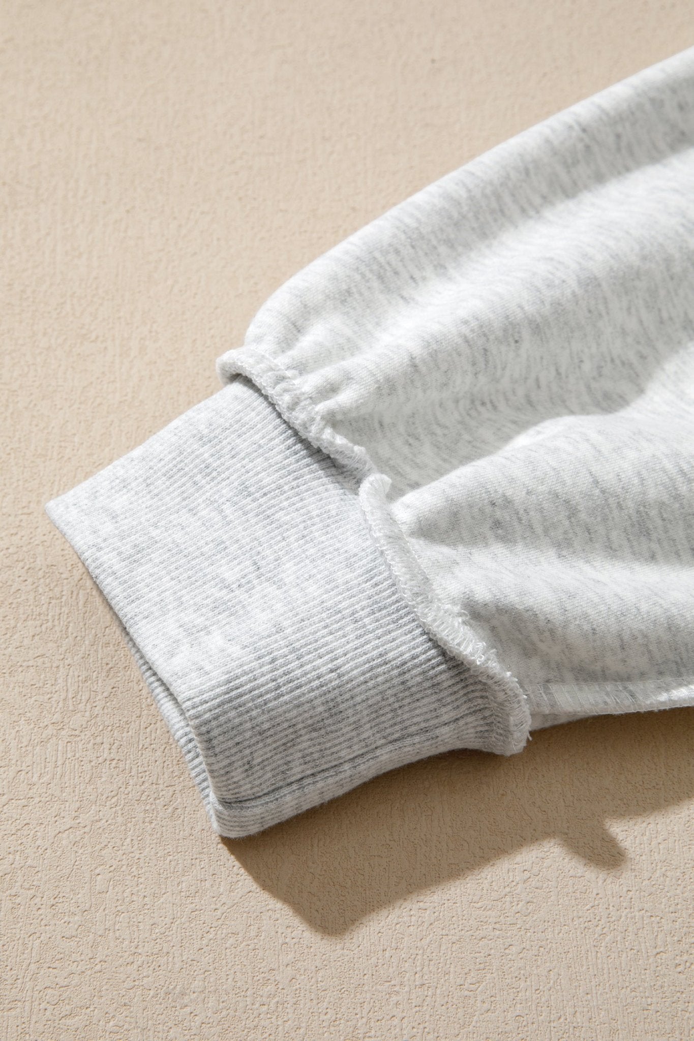 Close-up of light heather gray ribbed knit cuff on matching fabric against a warm beige textured background.