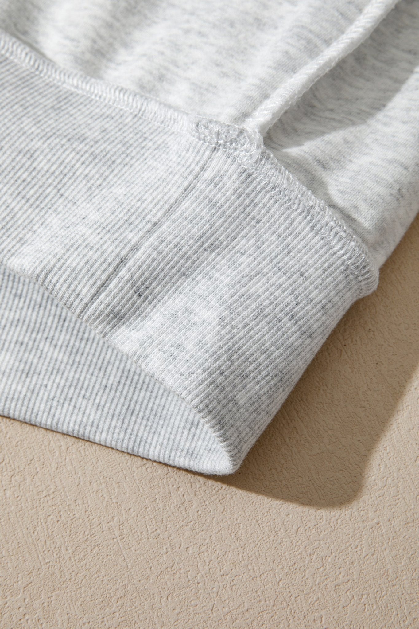 Close-up of light heather gray ribbed knit fabric with folded cuff detail on beige.