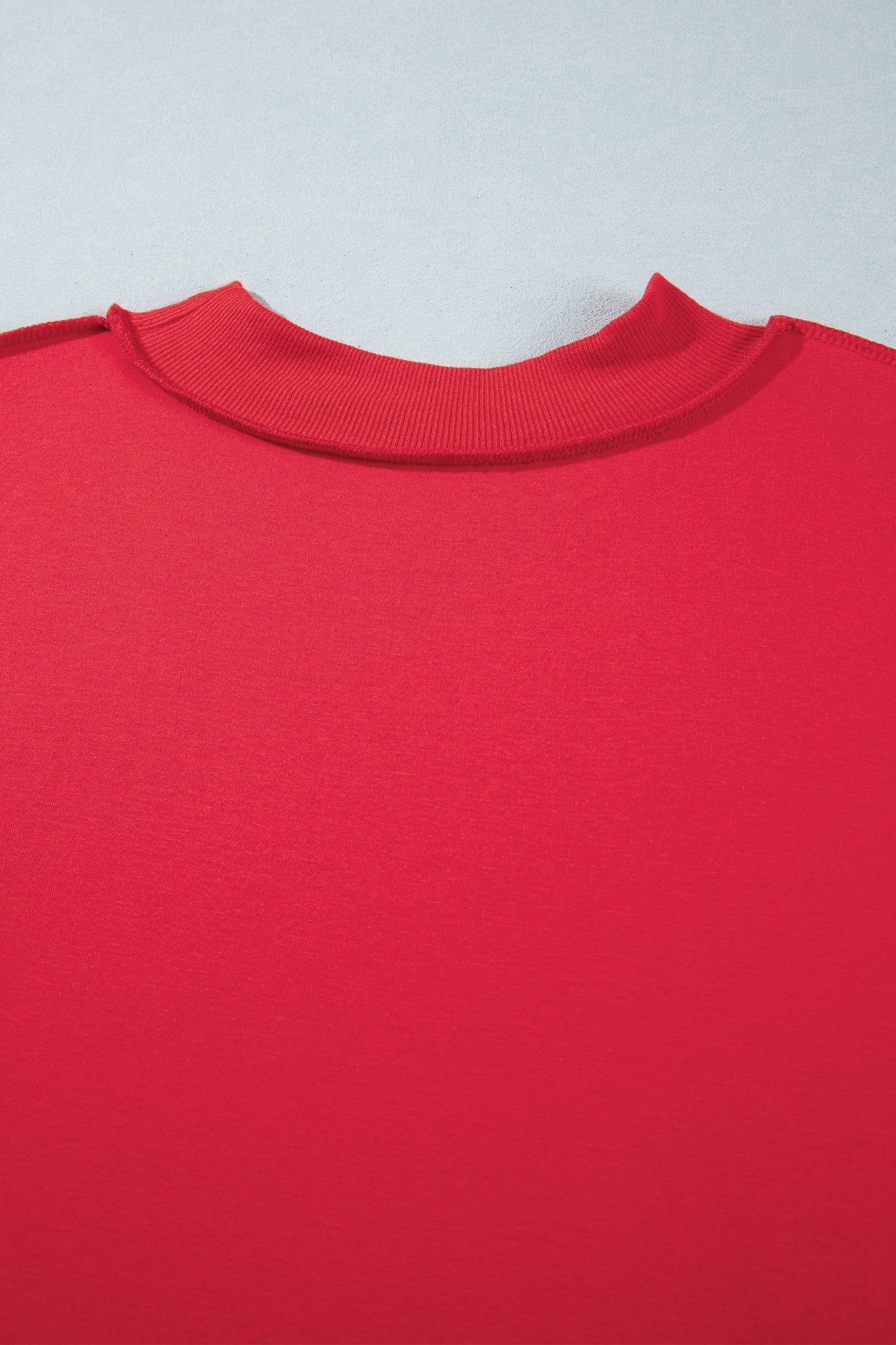 Close-up of bright red ribbed knit garment showing the back of a crewneck sweater on light gray.