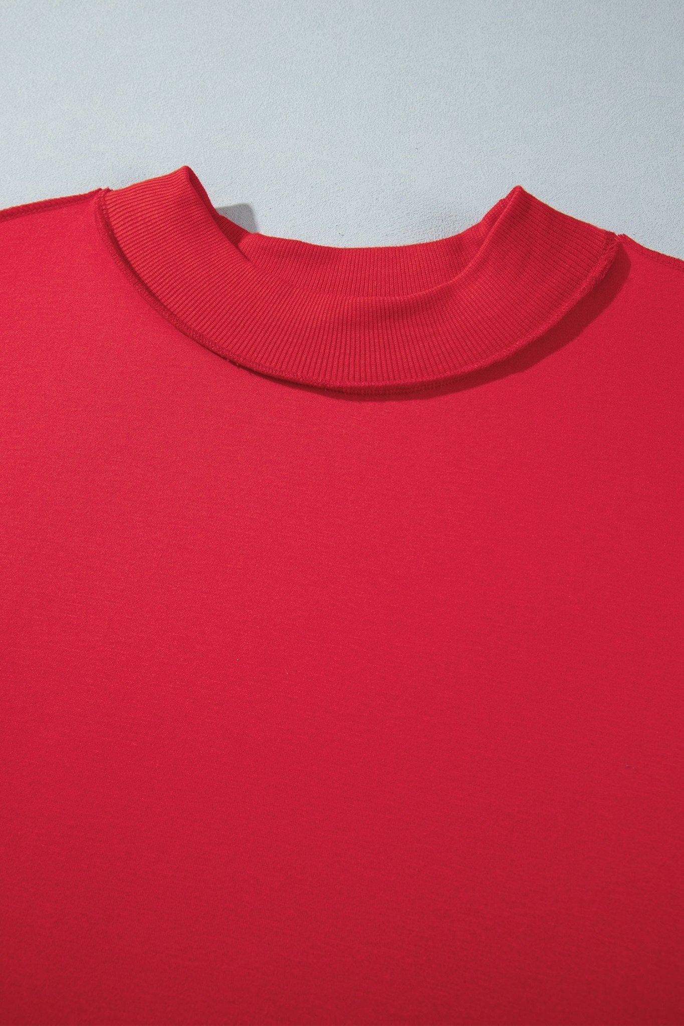 A close-up of a bright red knit top showing the ribbed mock neck collar against a light gray background.