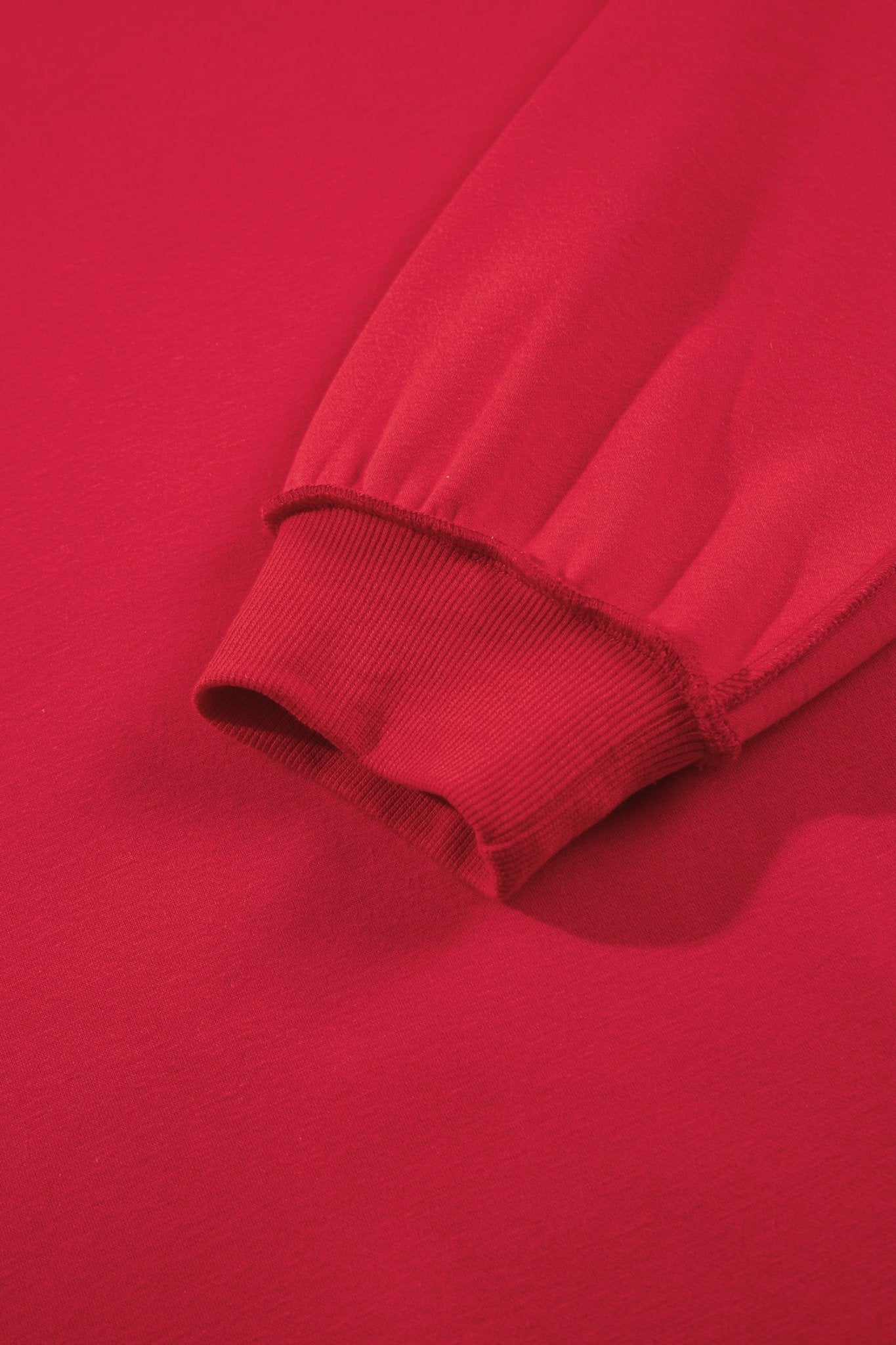 Close-up detail of a bright red sweatshirt sleeve cuff, showing the ribbed elasticized hem and fabric texture.