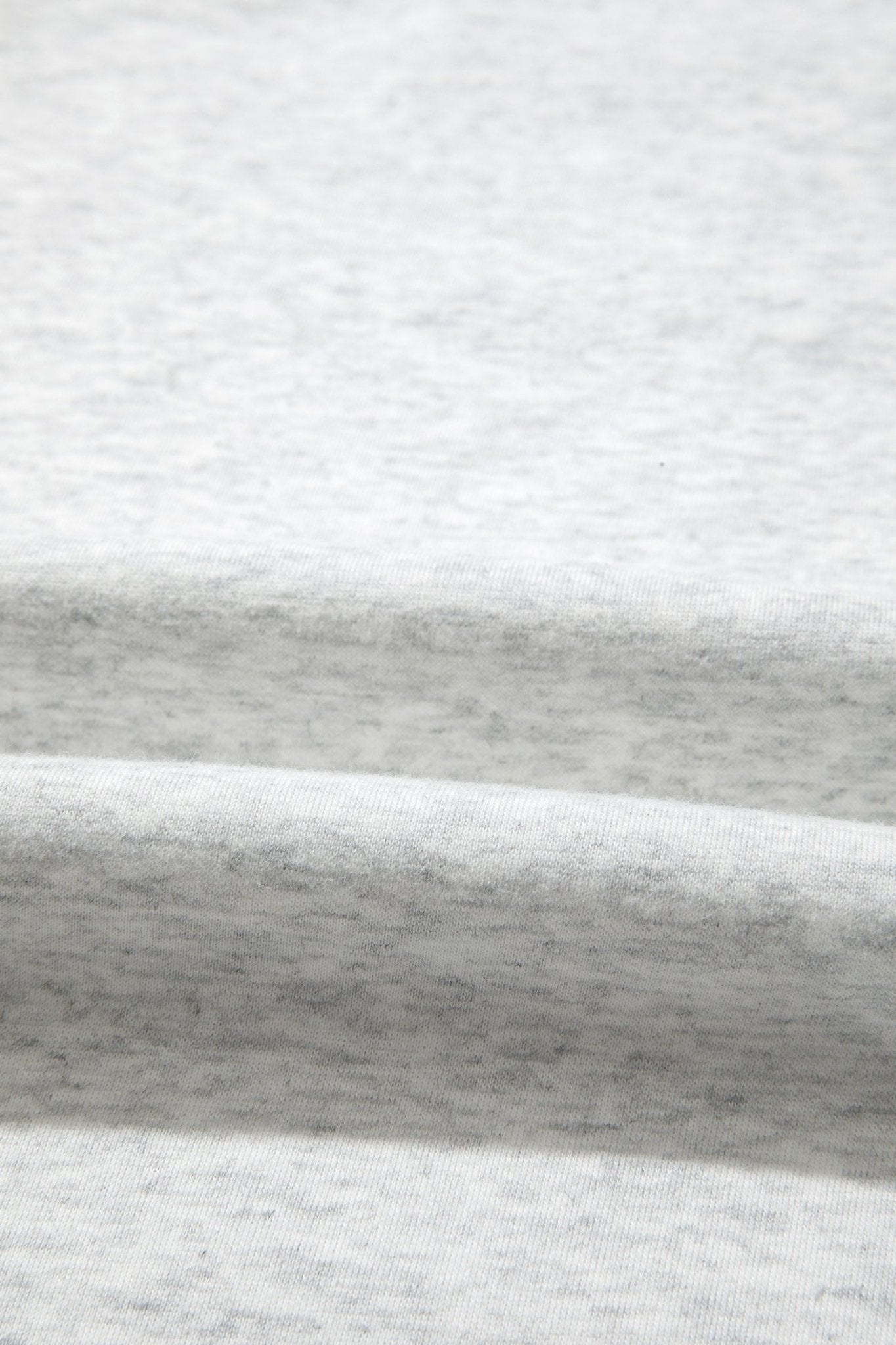 Close-up of a light heather gray fabric with soft folds showing the texture and color variation.
