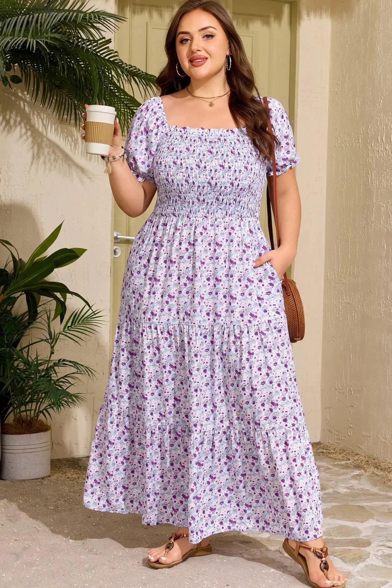 Woman in a floral dress holding a coffee cup outdoors.