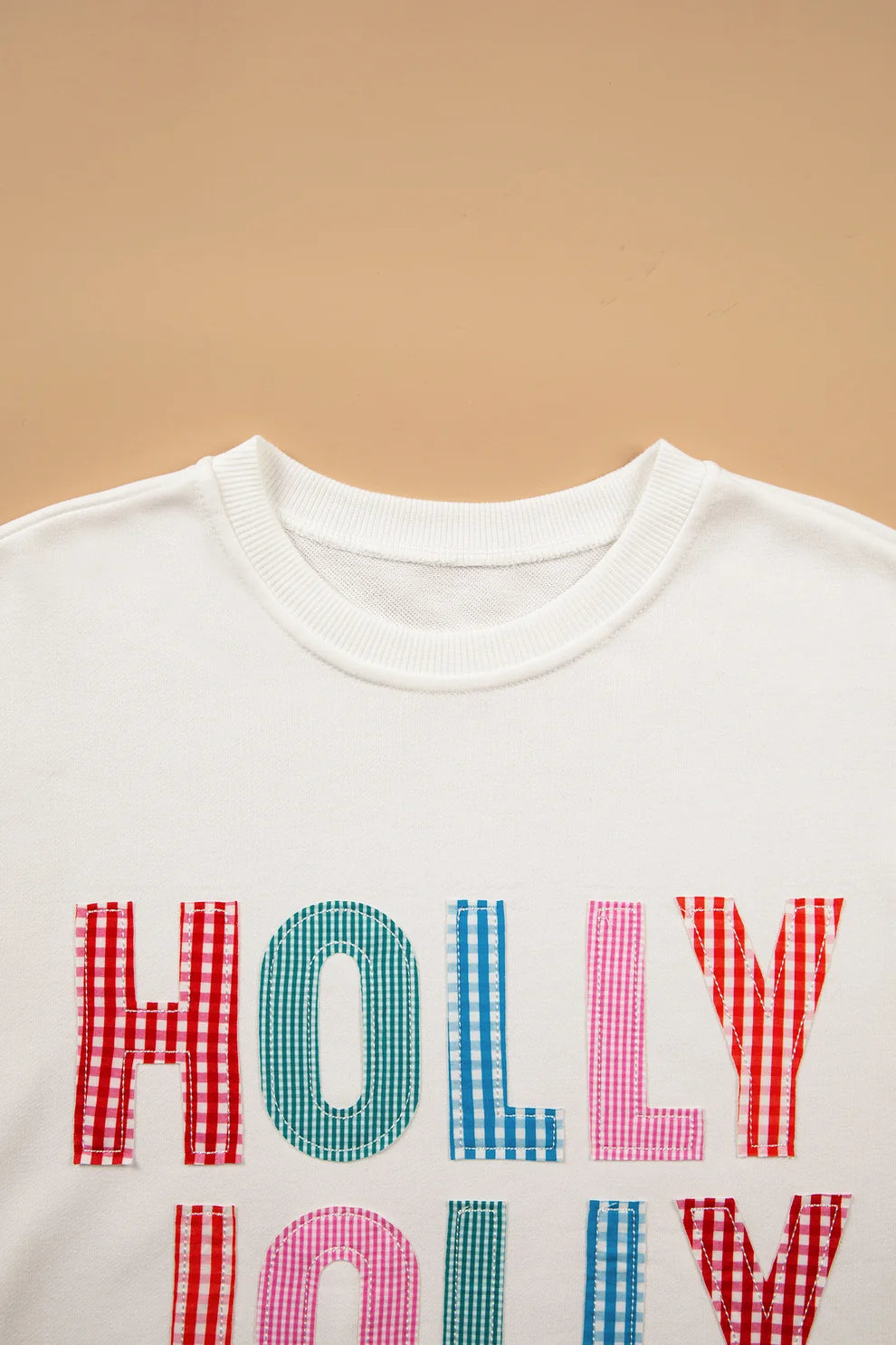 Close-up of red, blue and pink gingham Holly Jolly letters on a white sweatshirt