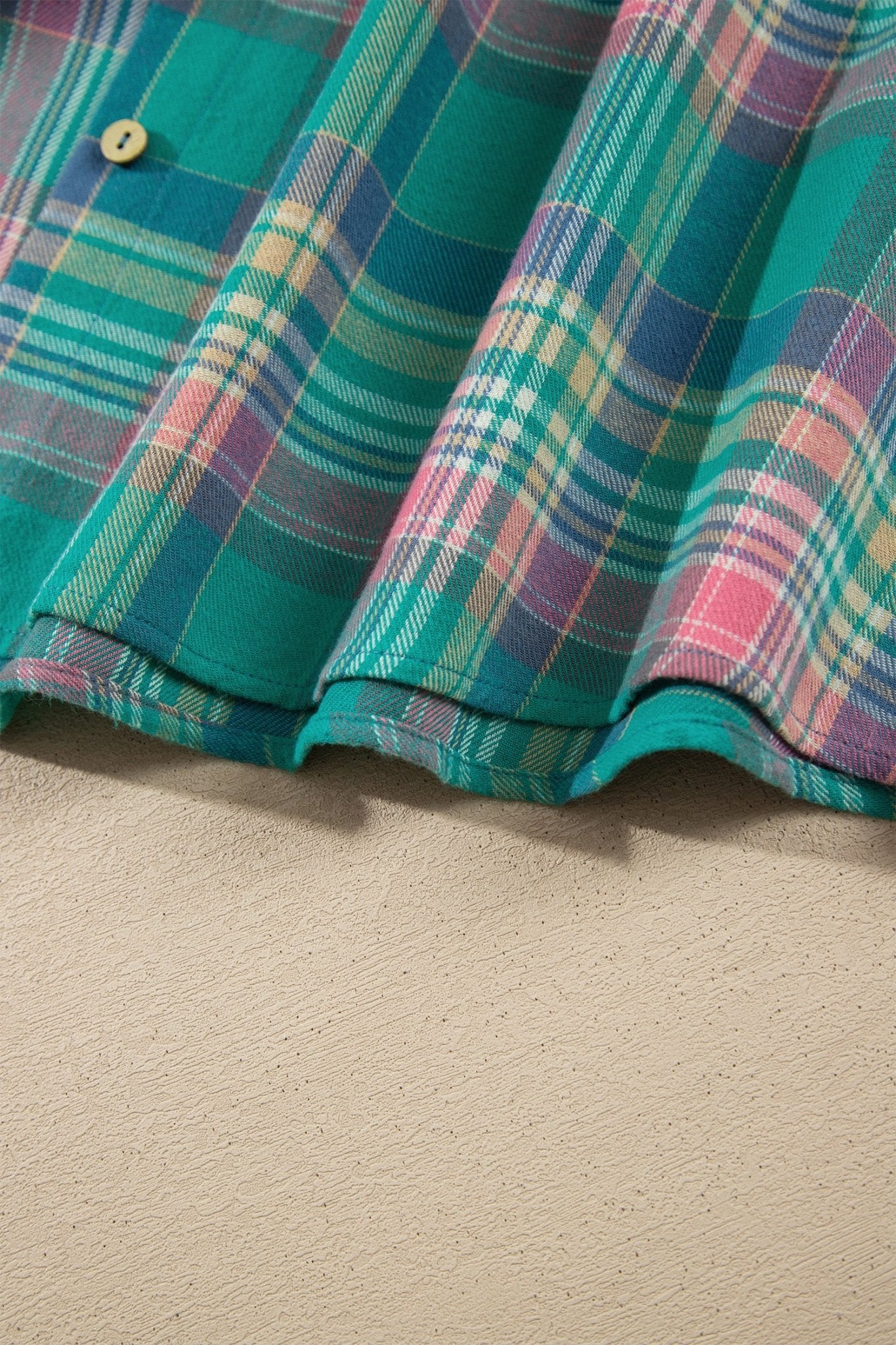 Teal, green, pink, and blue plaid fabric with a yellow button on textured beige.