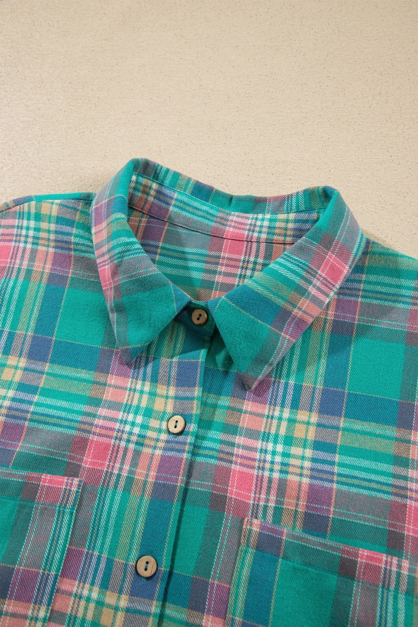 Plaid button-down shirt collar and chest in teal, pink, purple, and yellow on beige.