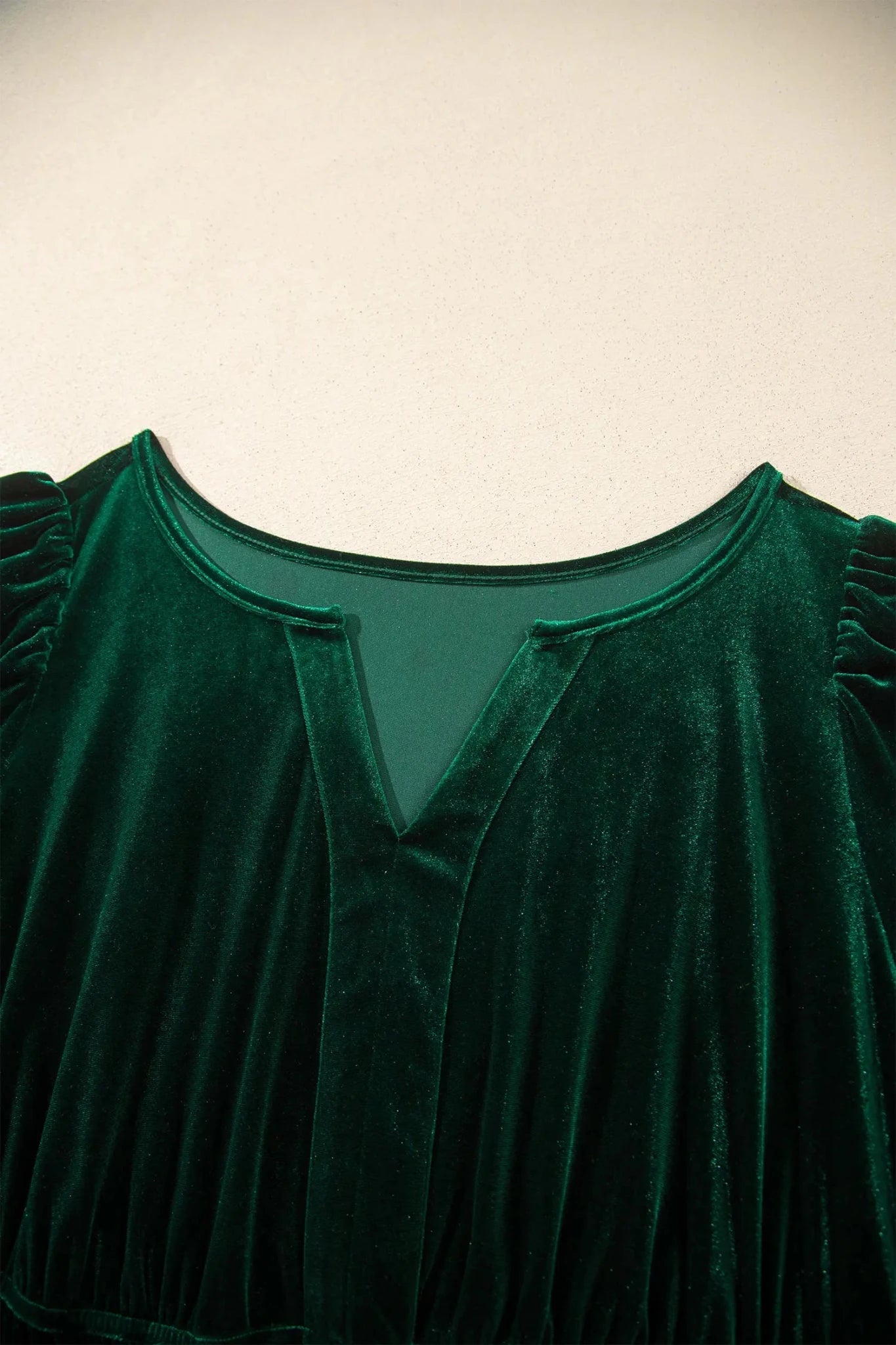 Close-up of dark green velvet top with split V-neck and ruffled shoulders.