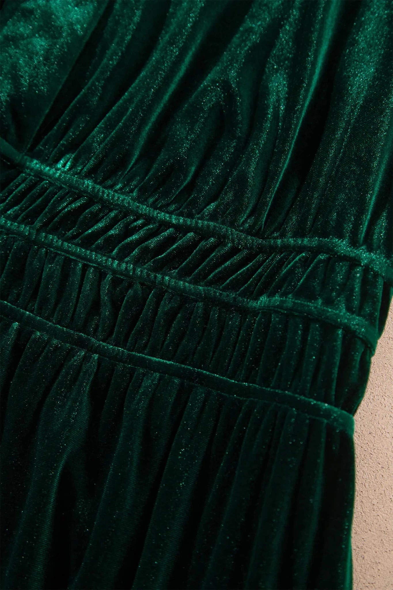 Close-up of a dark emerald green velvet garment with gathered pleats and a smocked waistband.