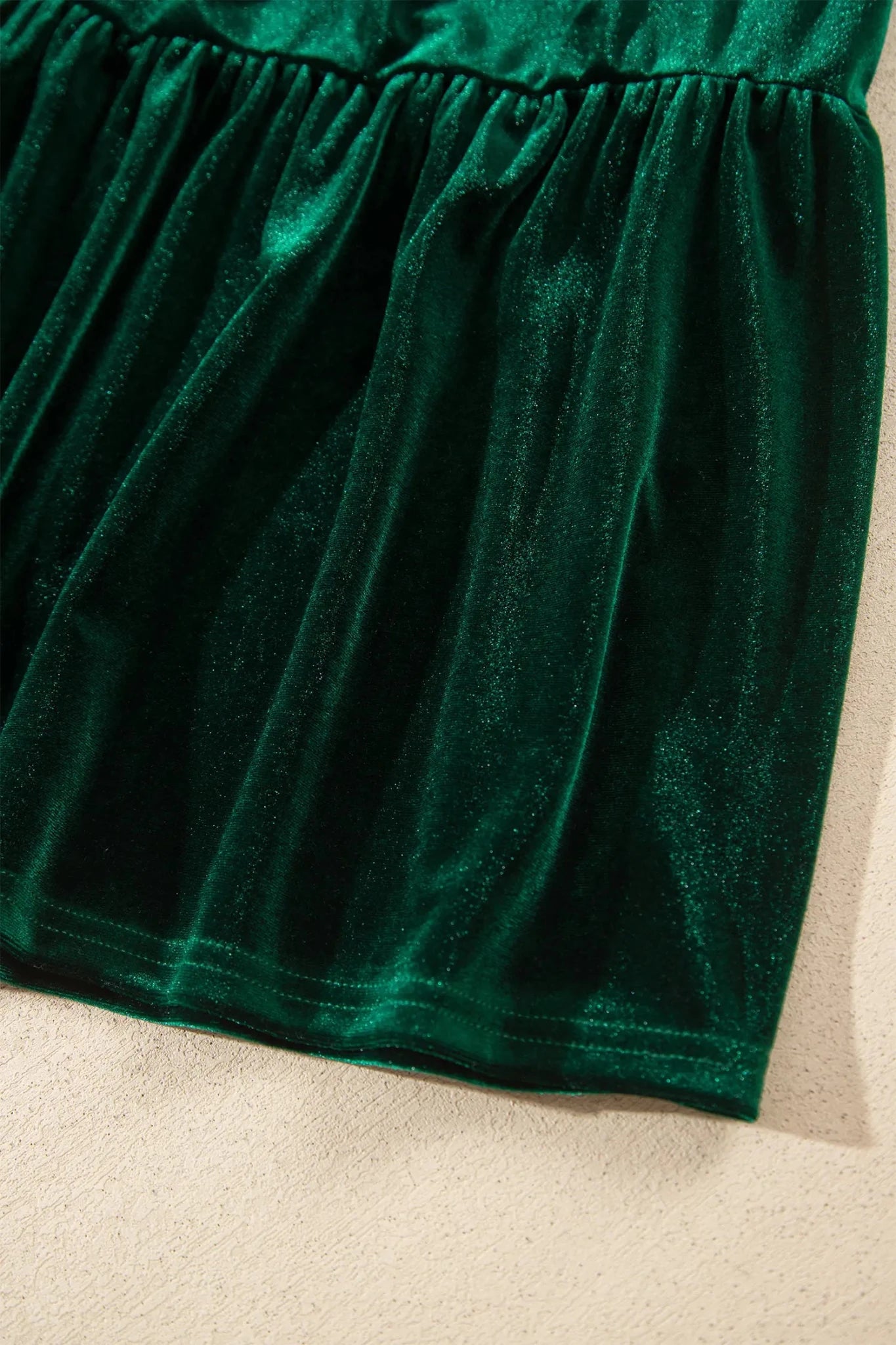 Close-up of emerald green velvet fabric with gathered waist seam.