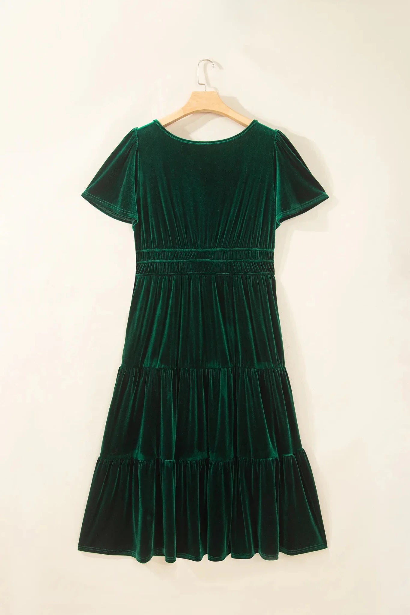 Dark green velvet tiered dress with flutter sleeves and smocked waist on hanger.