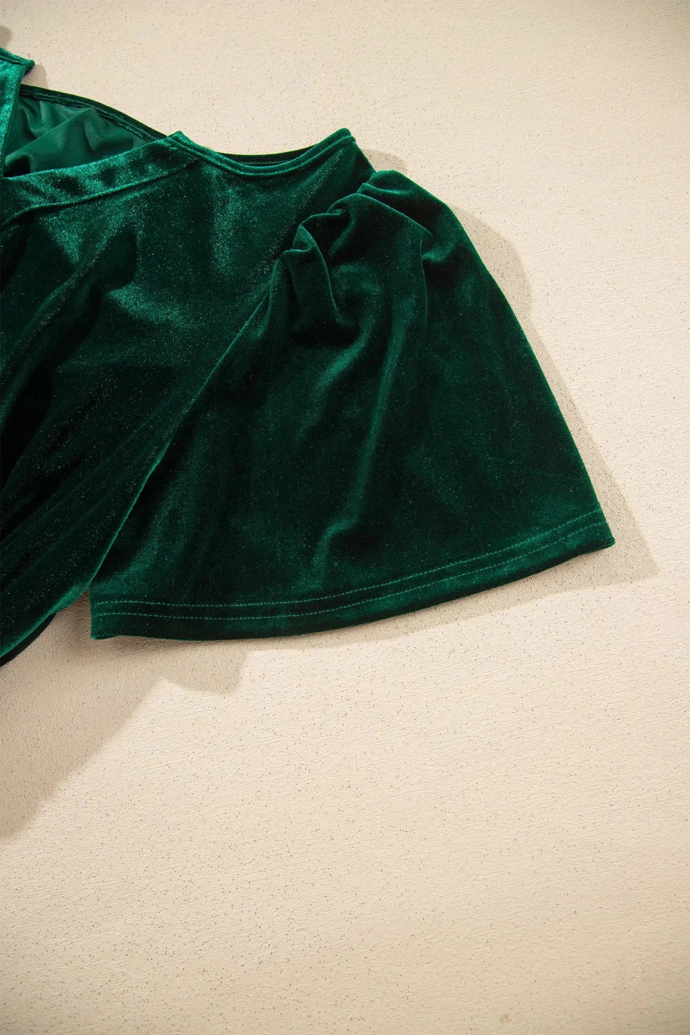 Close-up of dark green velvet garment with rich texture and draped folds.