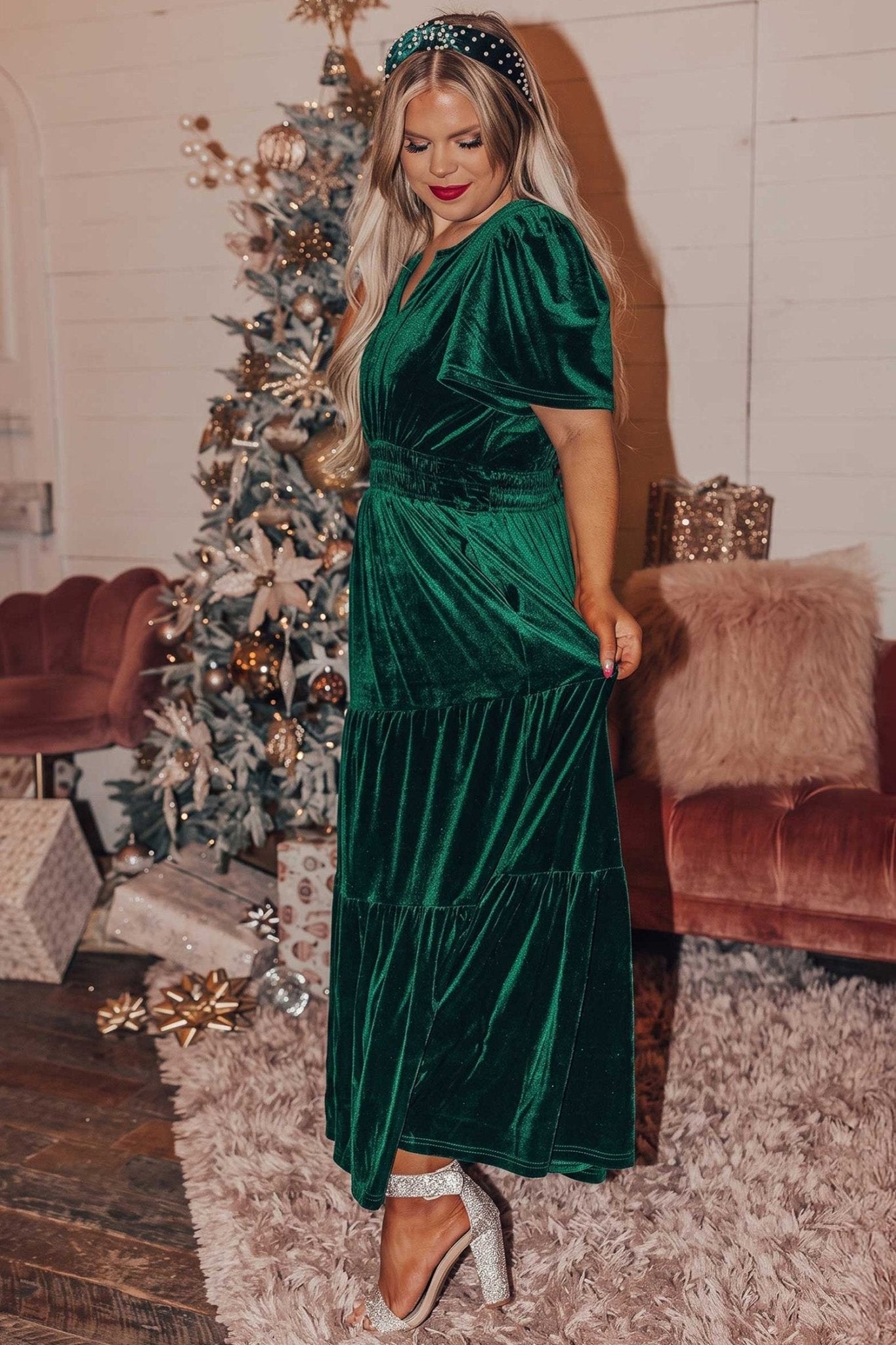 Woman in dark green velvet V-neck maxi dress with puff sleeves by Christmas tree.