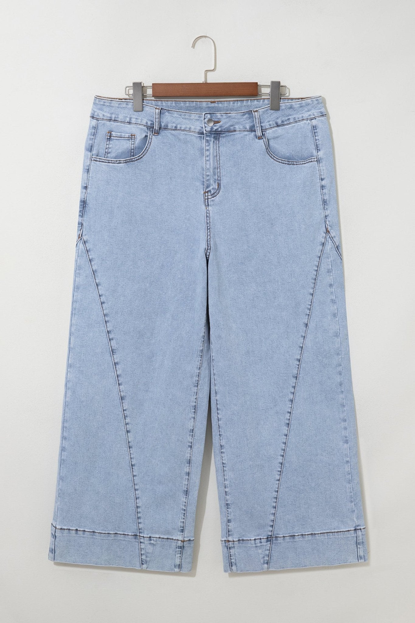 Light blue cropped jeans with diagonal seams on a wooden hanger.