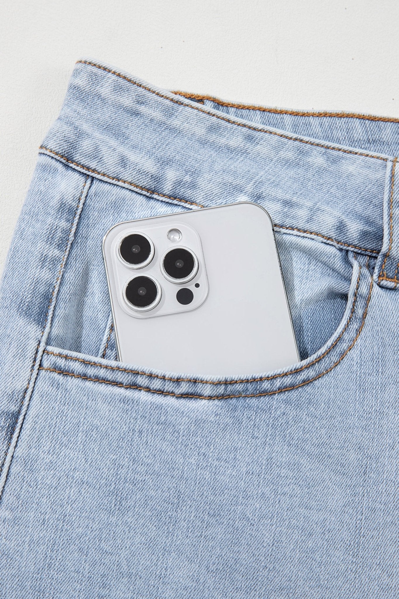 Silver smartphone tucked into the back pocket of light-wash jeans.