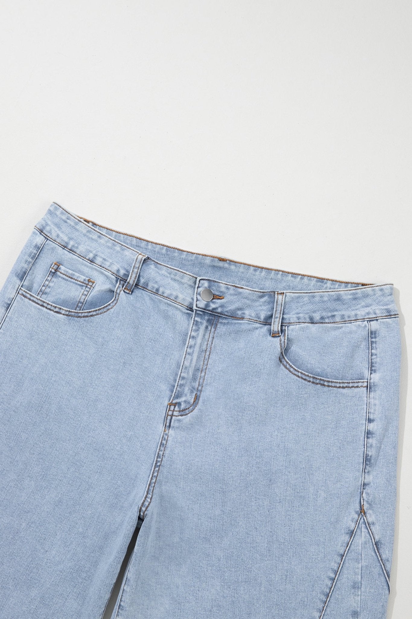Close-up of the waistband and front pockets of light-wash blue denim jeans on a plain light background.