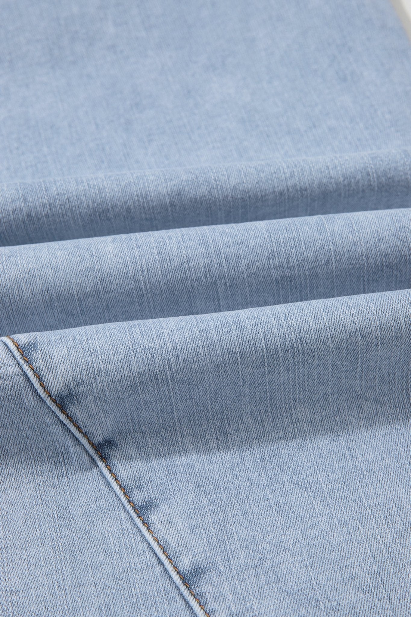 A close-up of light blue denim fabric with a diagonal seam and visible twill texture.