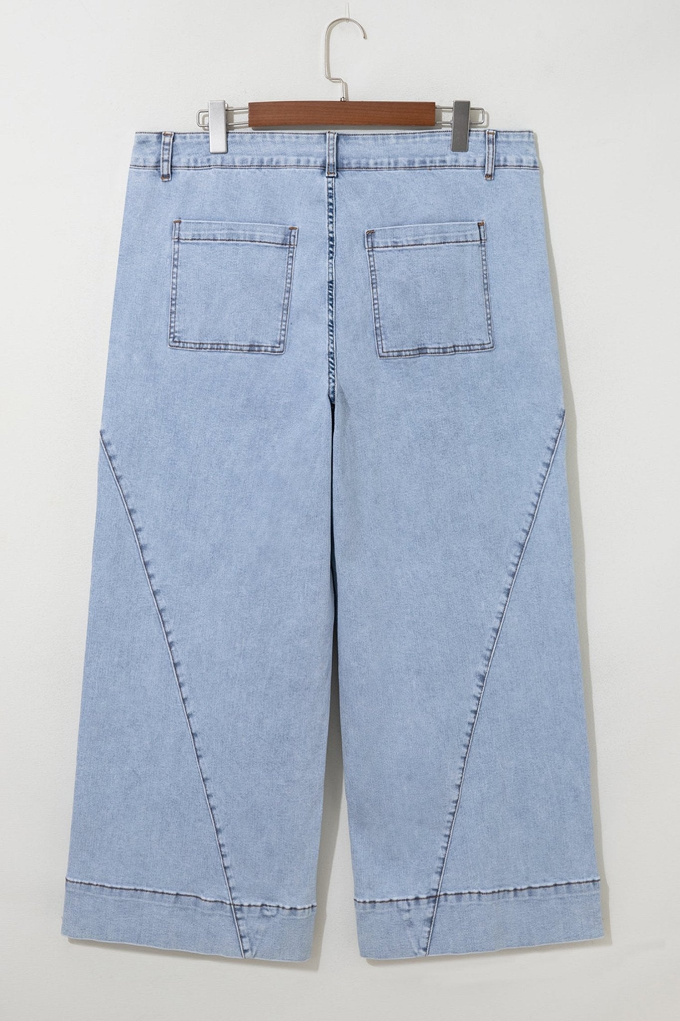 Light blue cropped jeans with diagonal seams on a wooden hanger.