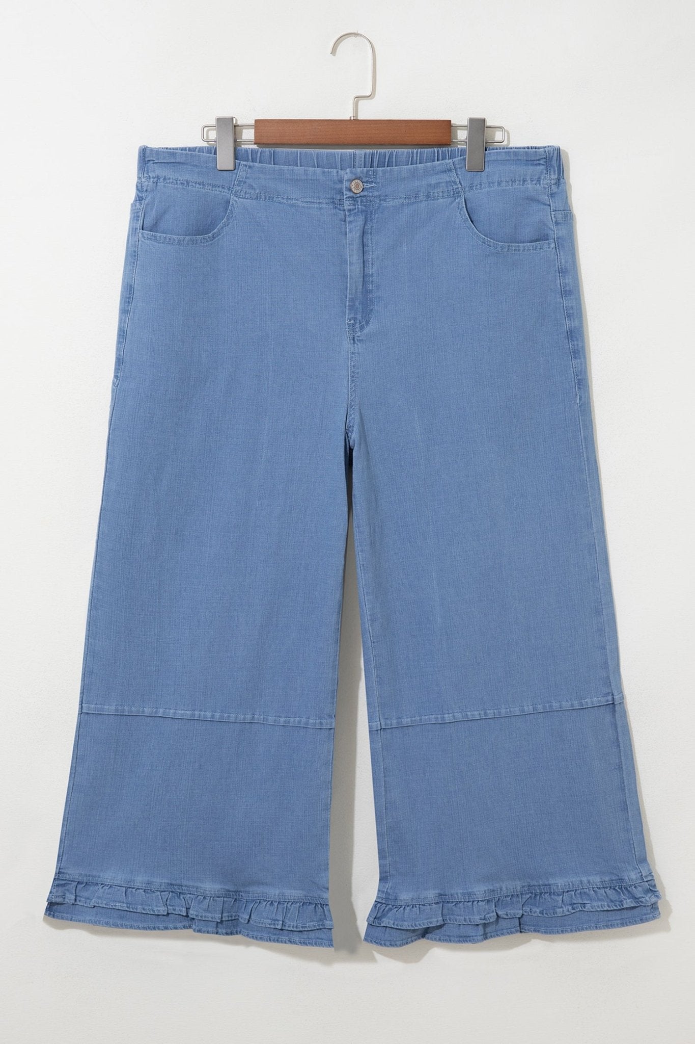 Light blue wide-leg denim pants with ruffled hems, hanging on a wooden hanger against an off-white background.