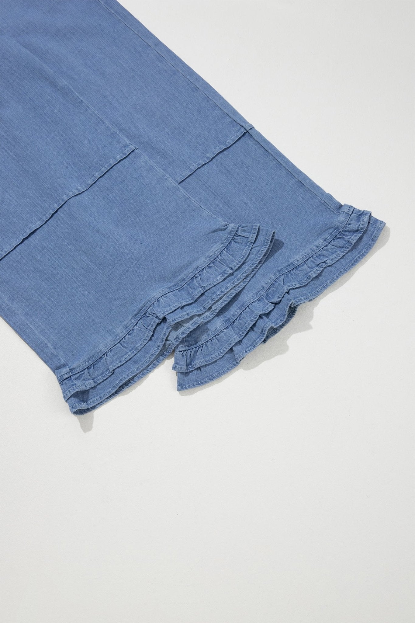 Close-up of blue denim pants folded on a light gray background, showing a ruffled hem detail.