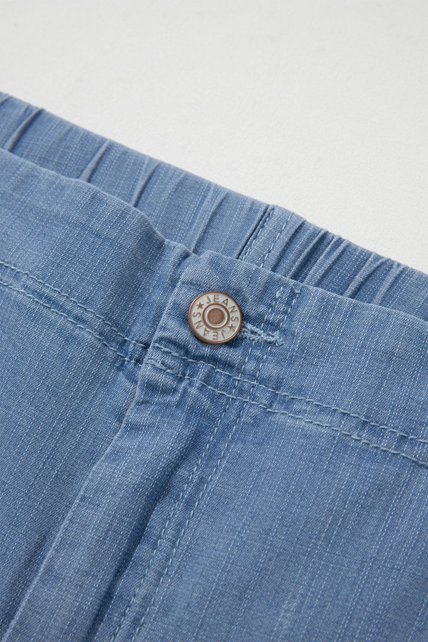 Close-up of blue denim shorts showing the waistband, elasticized gusset, and 'SOL'S' branded metal button.