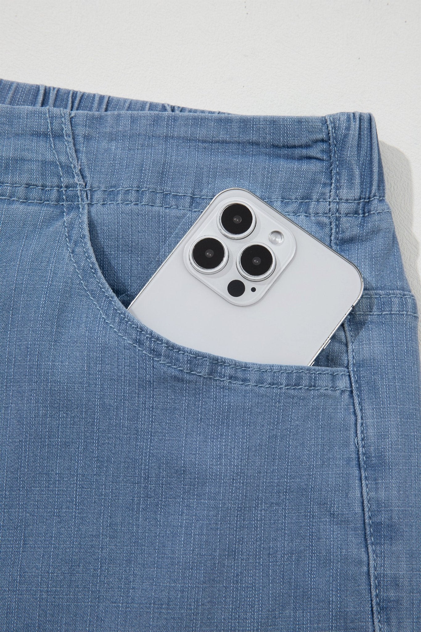 Close-up of a light blue denim pocket holding a white smartphone, shown against a plain light background.