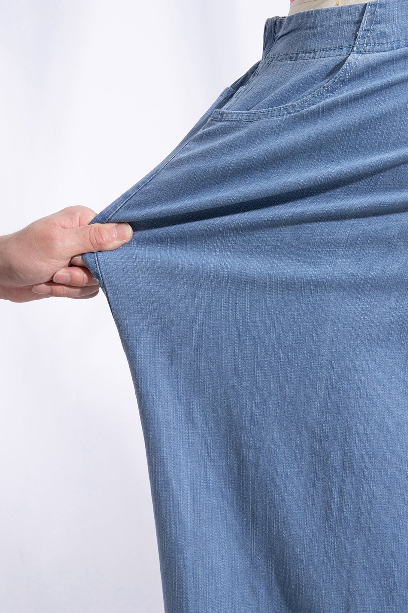 Close-up of a hand stretching light blue elastic pants against a white background.