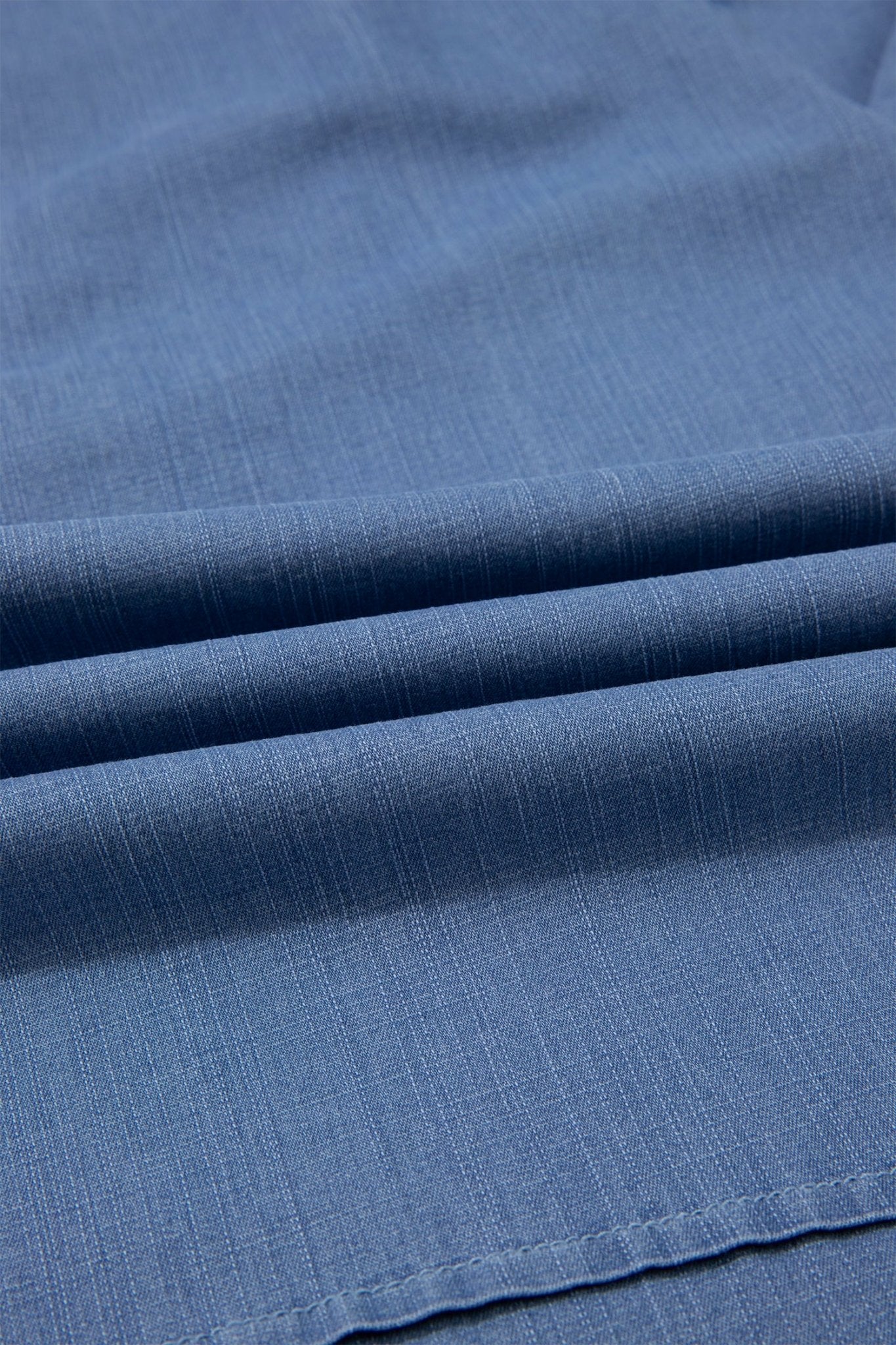 A close-up of blue woven fabric with a fine textured weave and soft folds.