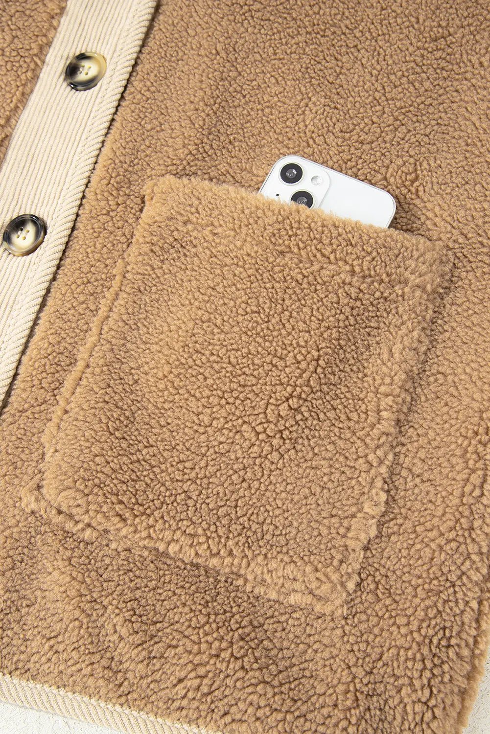 Close-up of a brown fleece jacket with a pocket containing a smartphone.