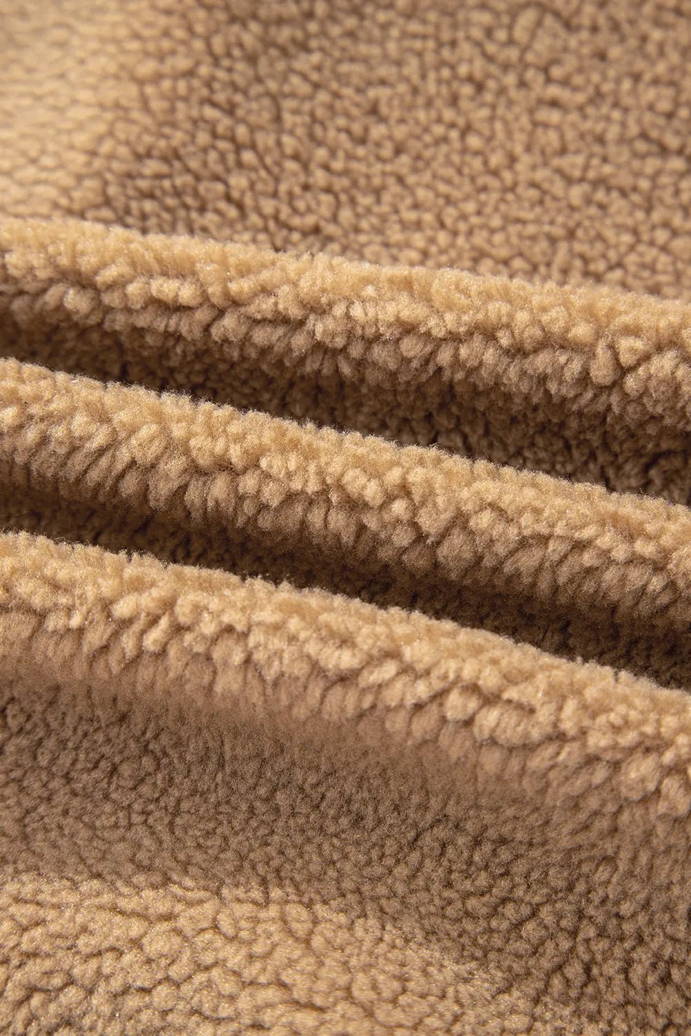 Close-up of a soft, plush fleece fabric in a warm tan or camel color, showing the textured loop pile and folded layers.