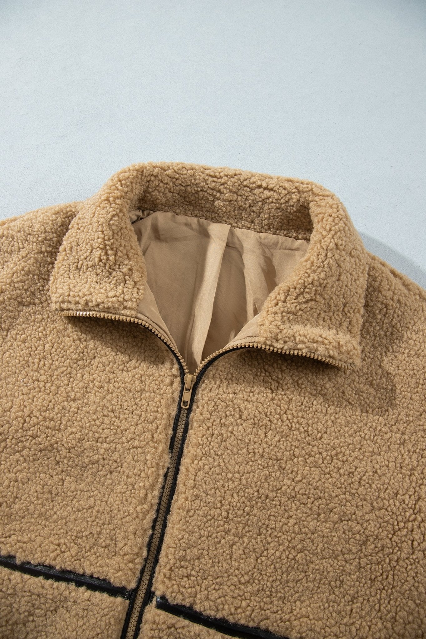 Close-up of tan sherpa fleece jacket with black zipper and beige lining.
