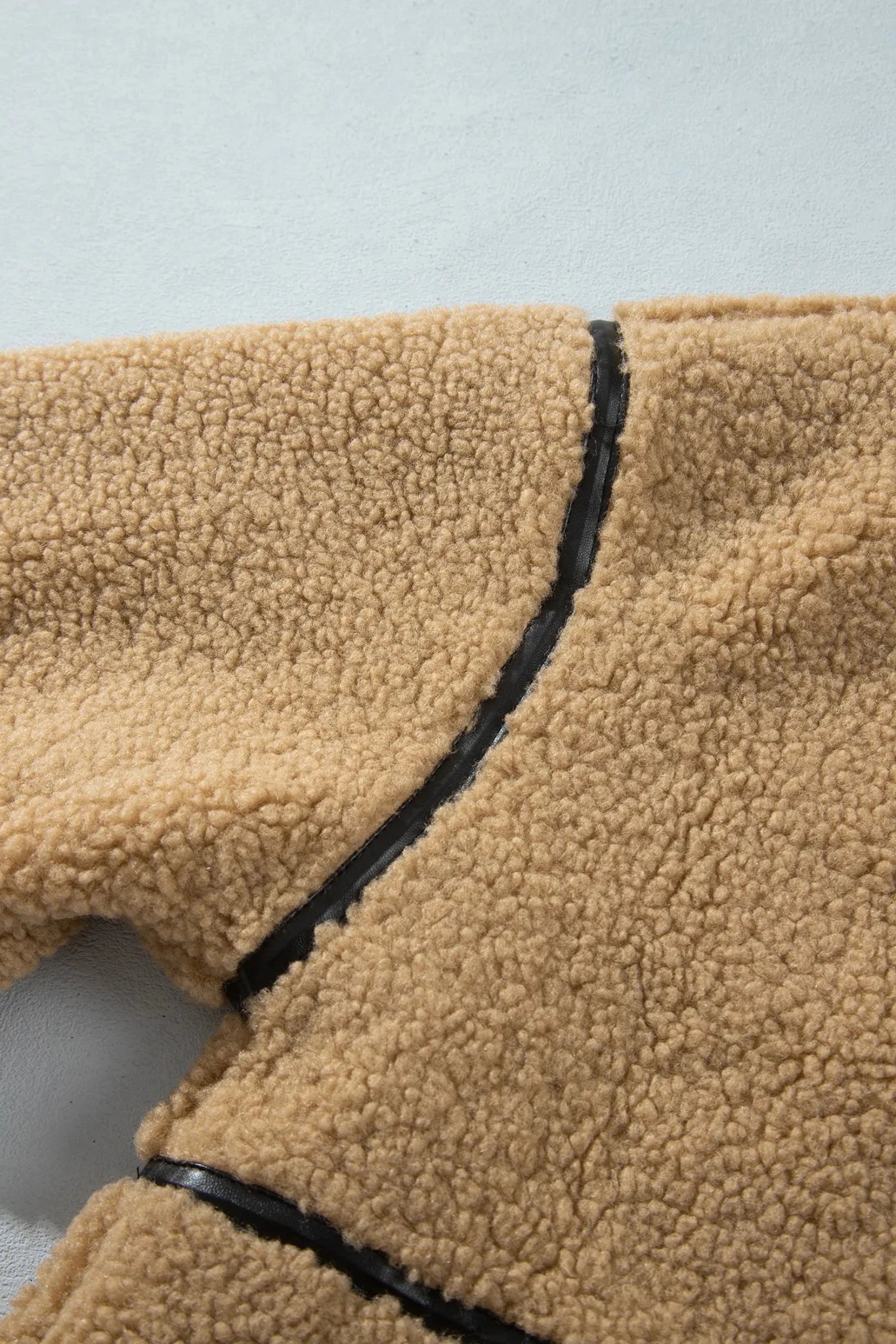 Close-up of tan sherpa fleece with black contrast stitching.