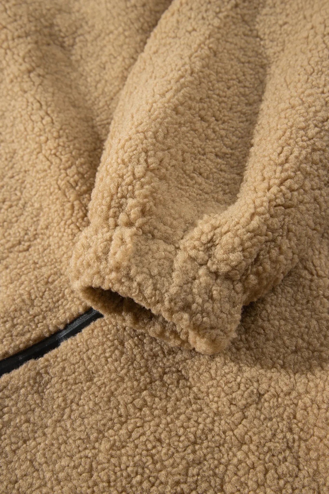 Close-up of a tan sherpa fleece garment, showing the soft textured fabric and a black zipper detail.