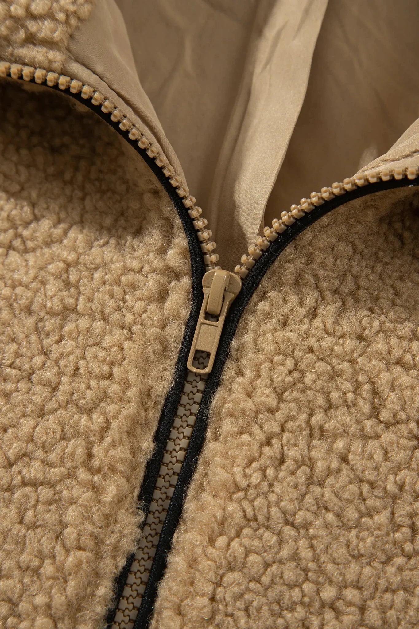 Close-up of beige sherpa fleece jacket with black zipper and gold pull.