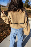 Back view of person in tan sherpa sweater with black piping and light jeans.