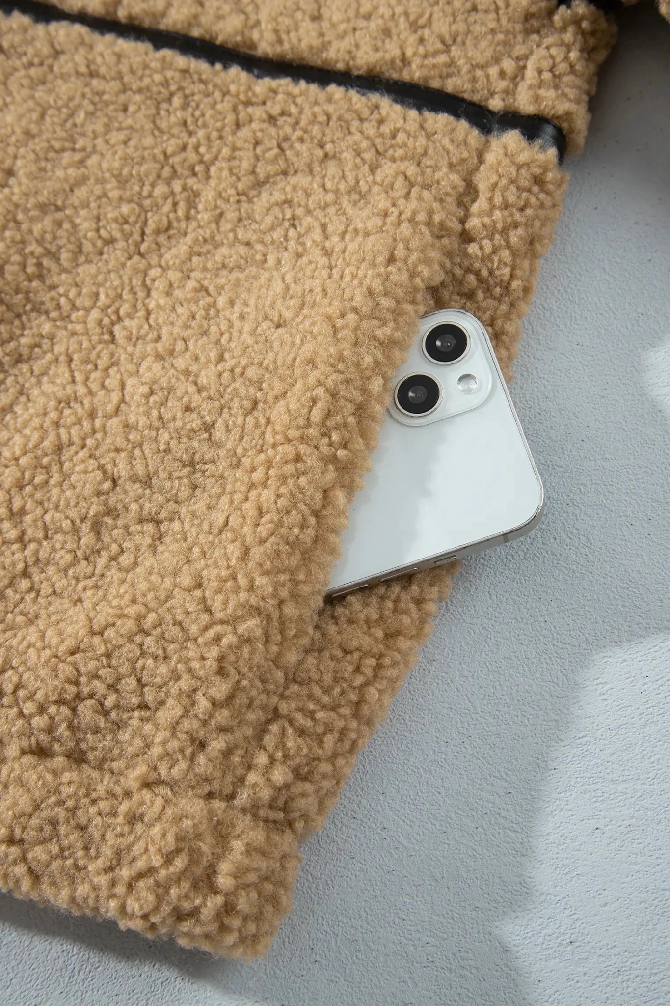 Close-up of tan sherpa pocket with white smartphone partially tucked inside.
