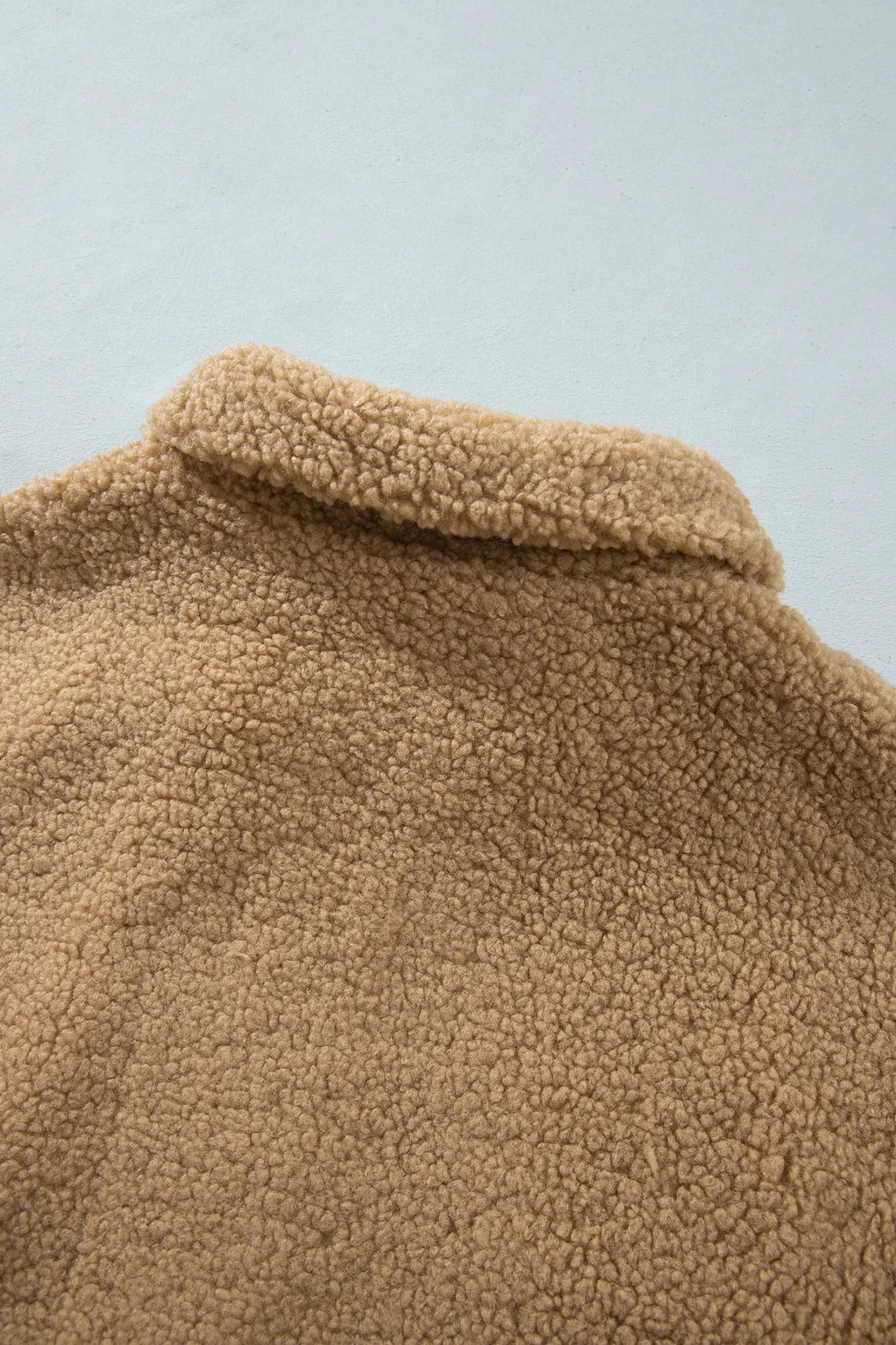Close-up of a tan sherpa fleece collar against a light gray background.