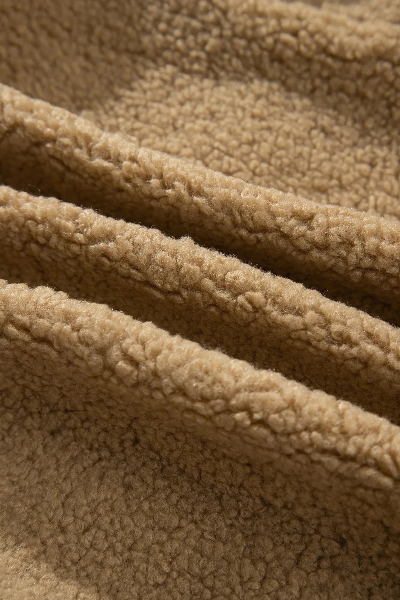 Close-up of soft tan sherpa fleece showing plush texture and folds.