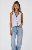 Woman wearing a white sleeveless top with black details and light blue jeans on a white background