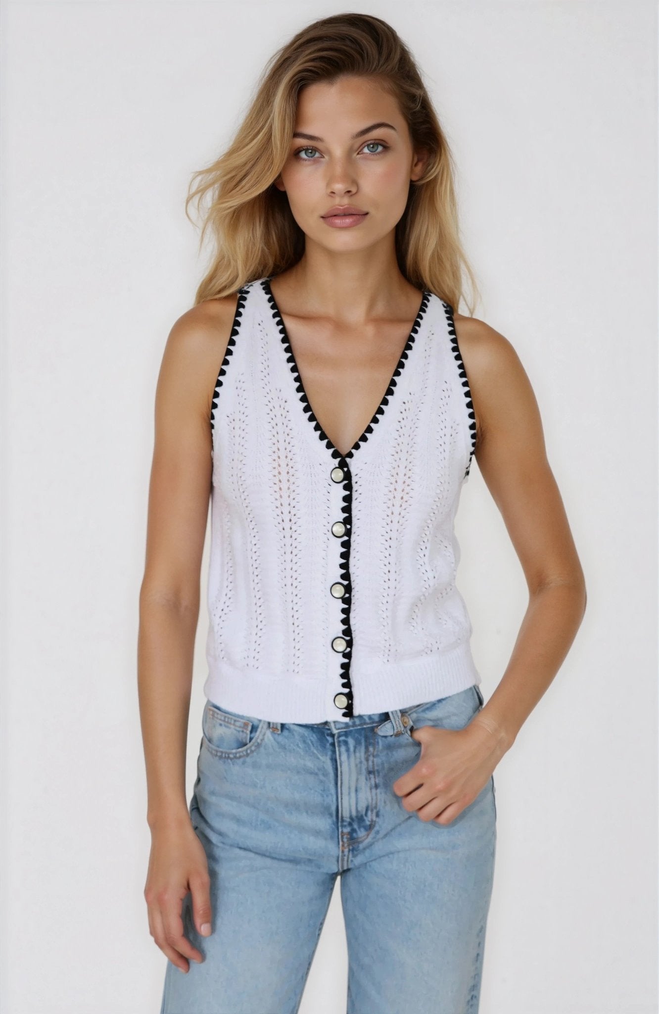 Woman wearing a white sleeveless top with black trim and blue jeans on a plain background