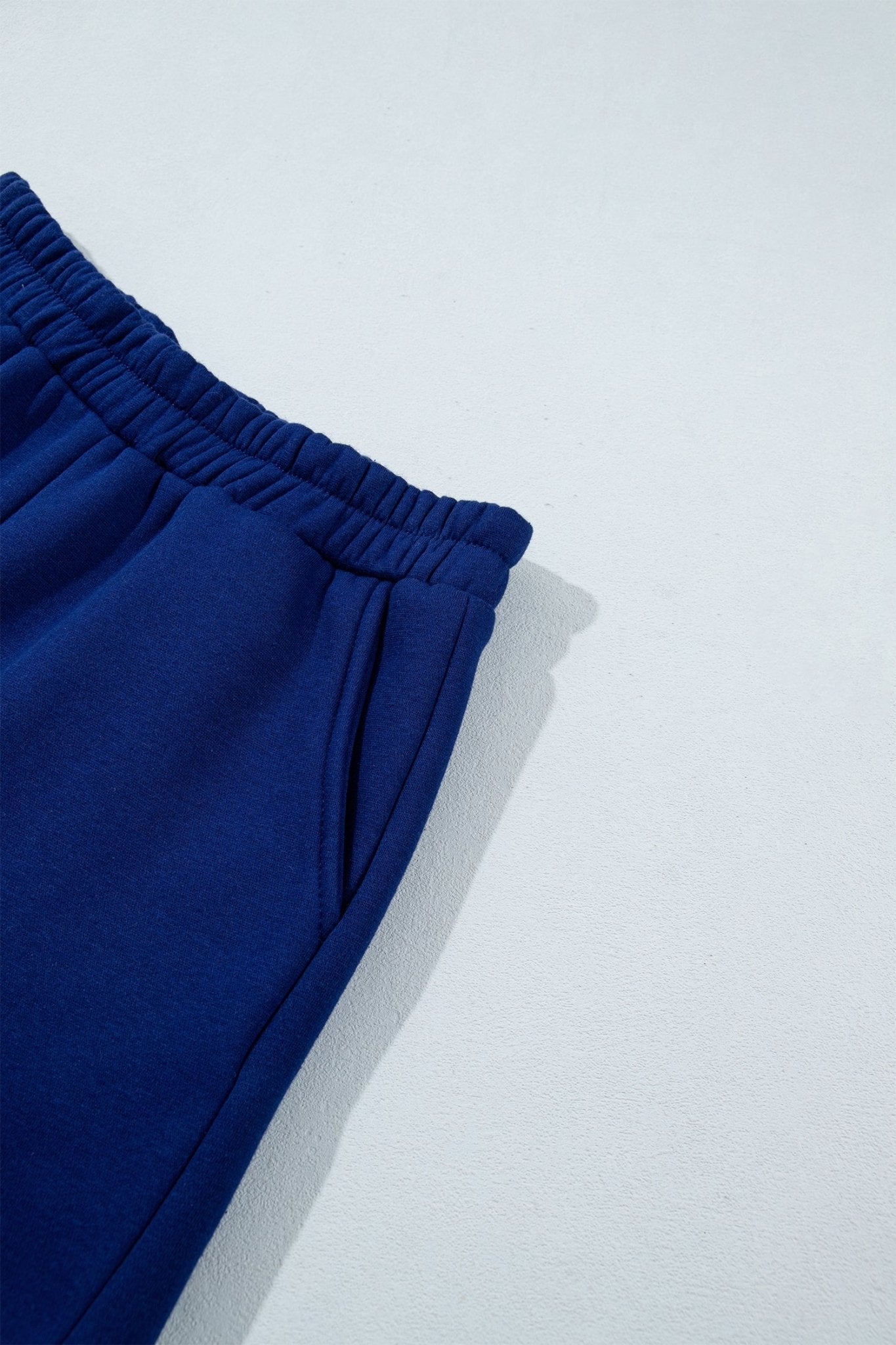 Close-up of royal blue sweatpants showing elastic waistband and side pocket against a light gray background.
