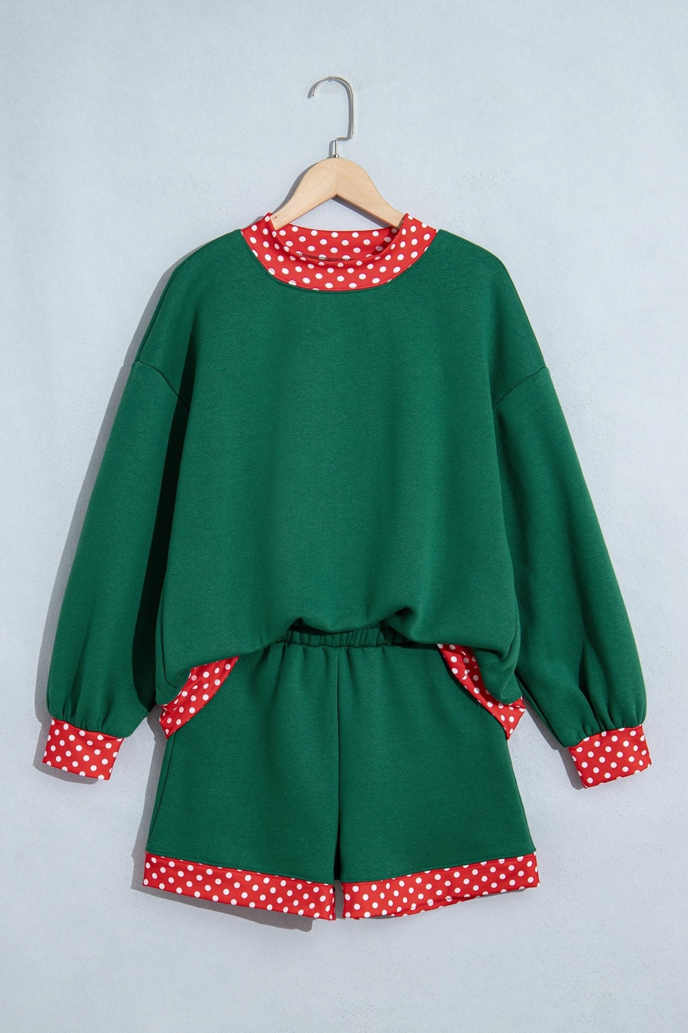 Green two-piece lounge set with sweatshirt and shorts, featuring red-white polka-dot trim on collar, cuffs, and hem.