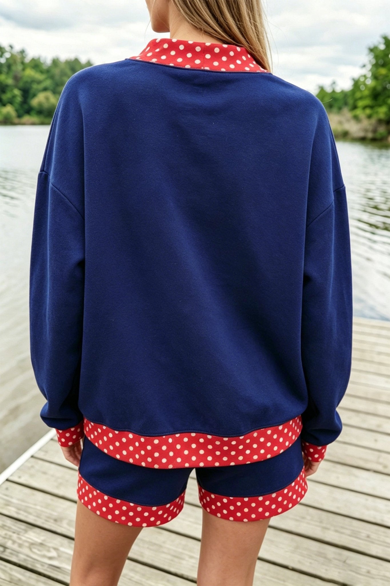 Person viewed from behind wearing navy blue lounge set with red-white polka-dot trim on a wooden dock.