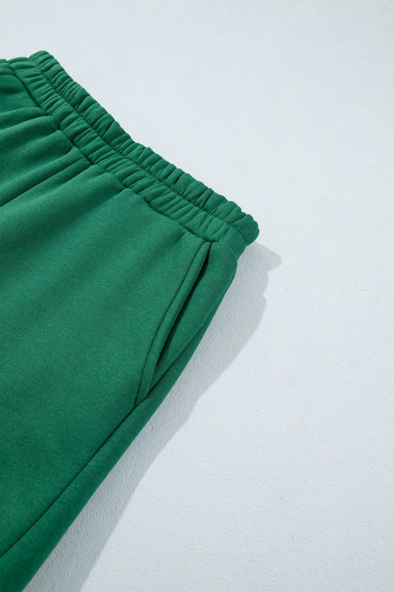 Close-up of bright green sweatpants with elastic waistband and side pocket against a clean white background.